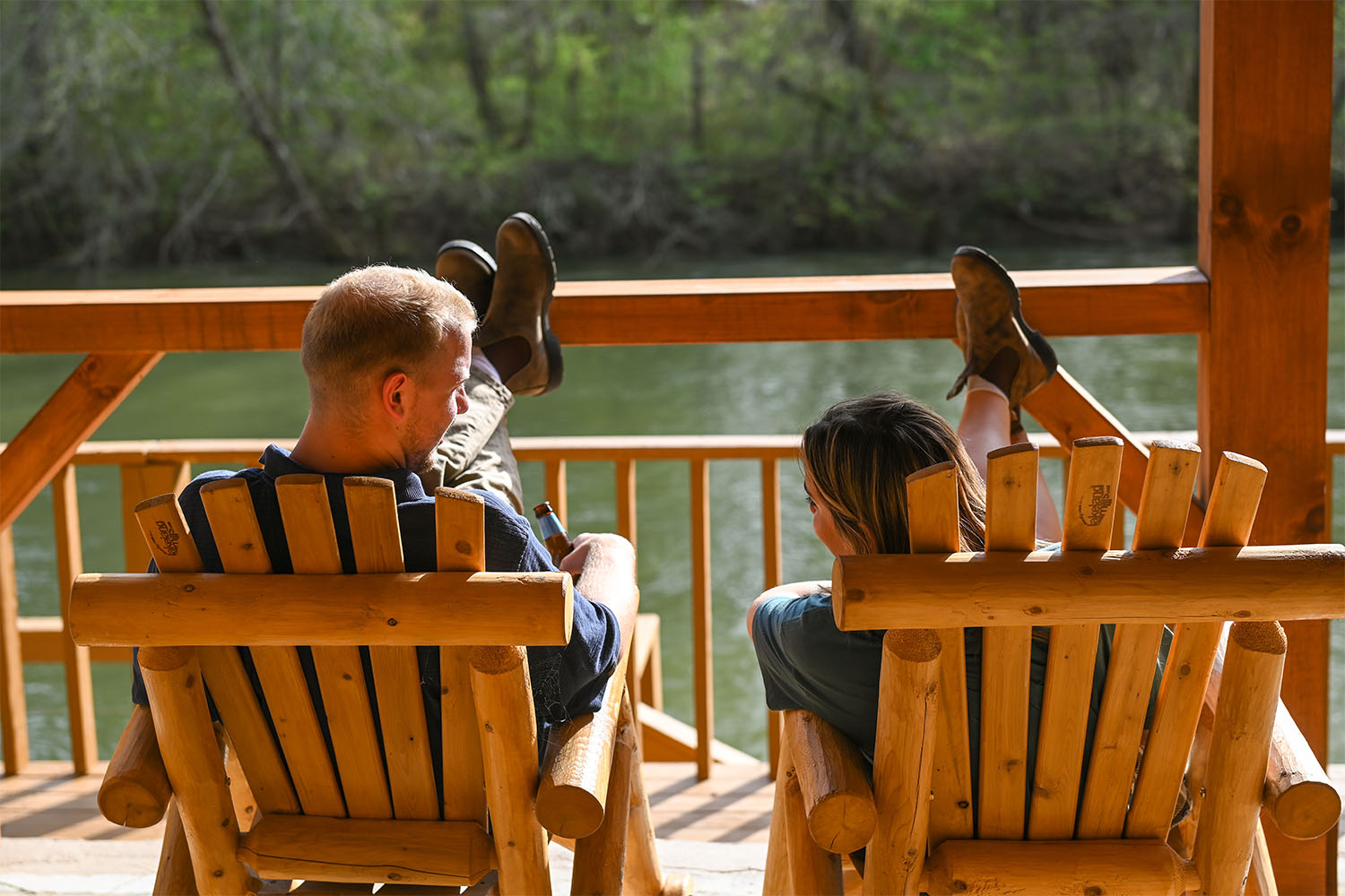 Two people sit in wooden chairs on the banks of the Ocoee River at Welcome Valley Village, a Timberroot Rustic Retreat